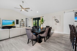A modern dining area with a dark wooden table, grey upholstered chairs, and a ceiling fan. - Spacious 4-bedroom house in serene Cape Coral (Cape Coral)