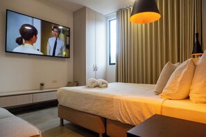Habitación de hotel con una cama, un televisor montado en la pared y una ventana con cortinas.