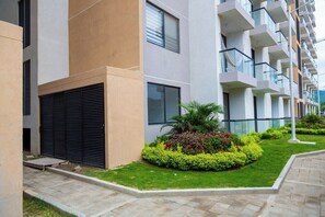 Un moderno edificio residencial de varios pisos con balcones, un jardín ajardinado y un paseo pavimentado.
