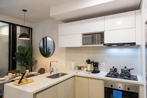 Una cocina moderna con armarios blancos, microondas integrado, estufa a gas y un lavamanos.