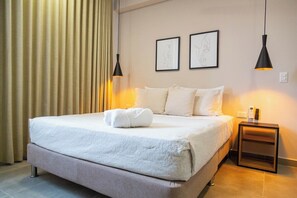 Ein Hotelzimmer mit einem großen Bett, zwei Nachttischen, einem an der Wand montierten Fernseher und einem Vorhang.
