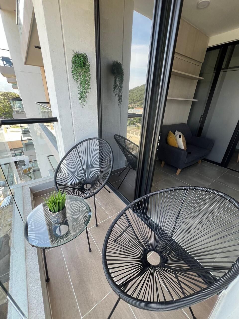 A balcony with two chairs, a small table with a plant, and a sofa with cushions.