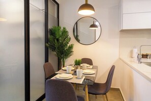 A modern dining area with a glass table, grey chairs, a potted plant, and a round mirror on the wall. - Apartamento familiar en Gaira con vista al jardin (Gaira)