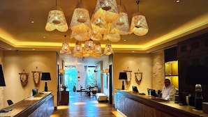 Um saguão de hotel com balcão de recepção, piso de madeira e luminárias pendentes.