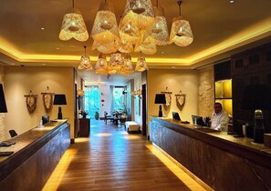 Una hall d'hotel con reception, pavimento in legno e lampade a sospensione.