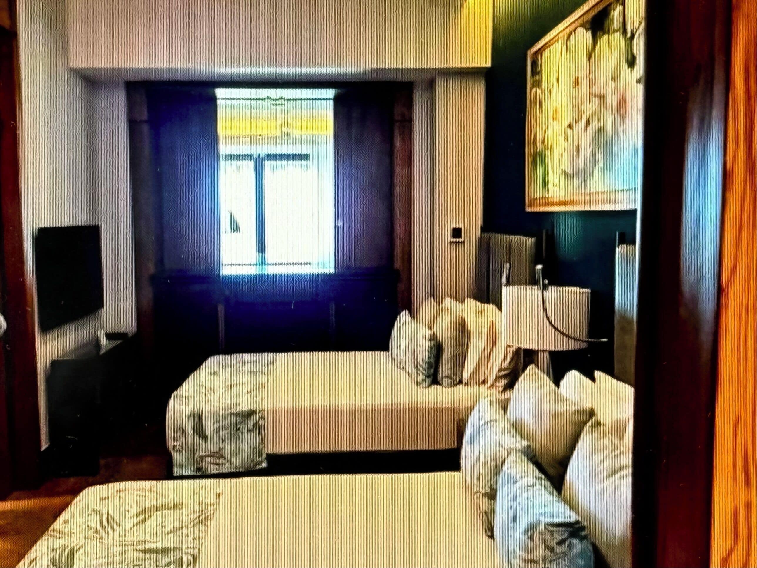 A room with a bed, a television, a window with curtains, and a painting on the wall.