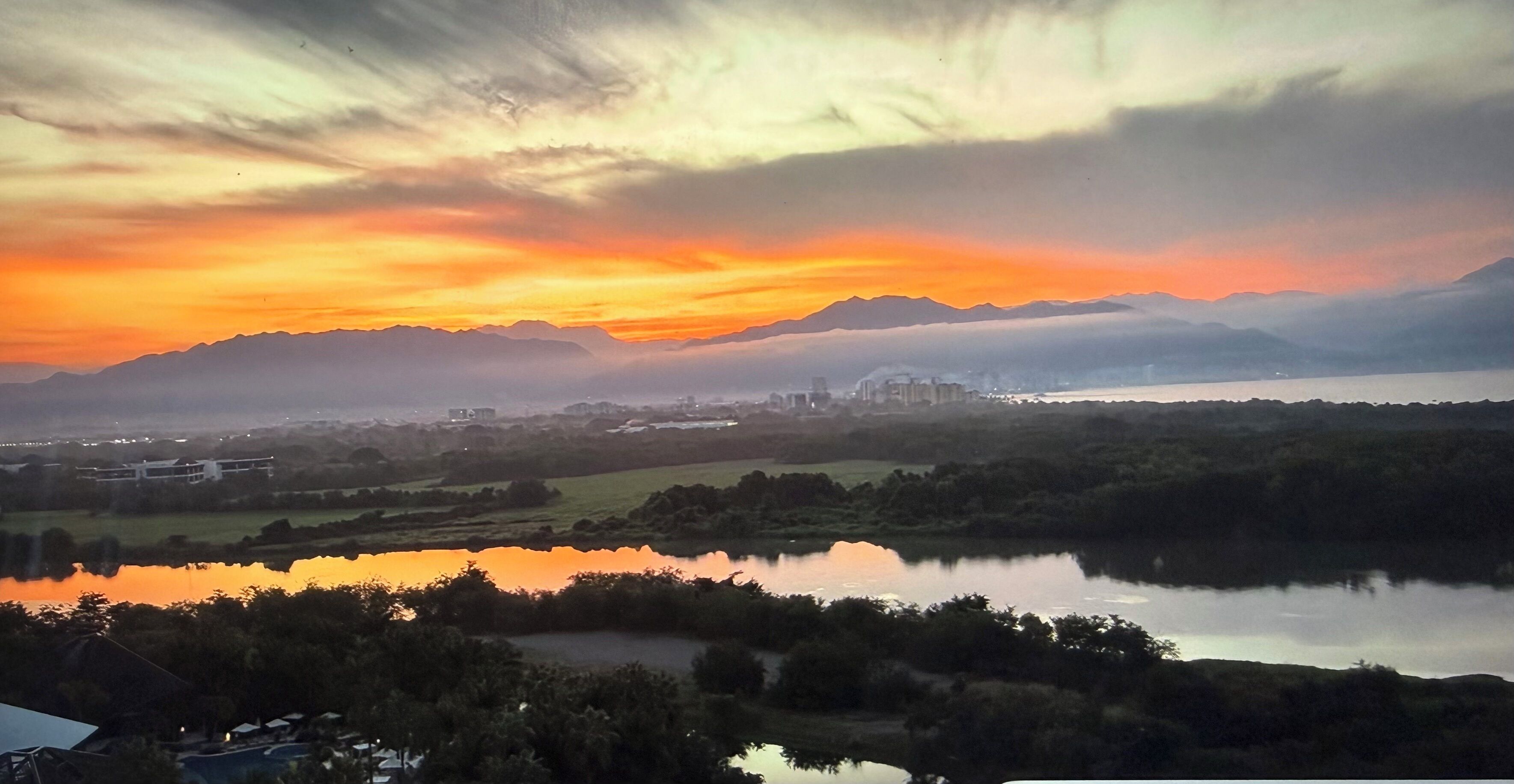 Un paisaje con una masa de agua que refleja el cielo, rodeado de vegetación y montañas distantes.