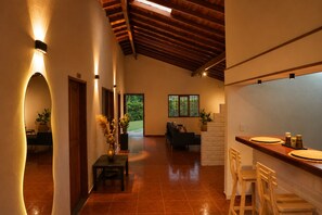 Un hall d’entrée spacieux avec un plafond en bois, un coin salon avec un canapé et un coin repas avec un comptoir et des tabourets.