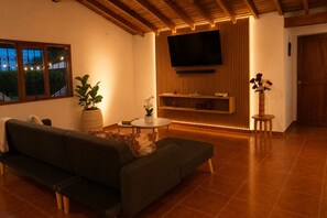 A modern living room with a sofa, a round coffee table, a TV mounted on a wooden wall, and a potted plant. - A country home perfect for families, nature, and luxury, just 5 minutes from the airport (Antioquia)