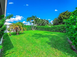 A well-maintained lawn with a variety of trees and shrubs, a clear blue sky, and a building in the background. - Exquisite Oasis Home! ~ Close To Beach & Shops! (Fort Lauderdale)