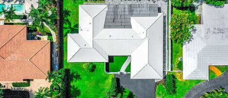 Vue aérienne d’une propriété résidentielle comprenant une grande maison, une piscine et des jardins bien entretenus.