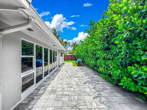 A pathway leading to a building with large windows and a hedge on one side. - Exquisite Oasis Home! ~ Close To Beach & Shops! (Fort Lauderdale)