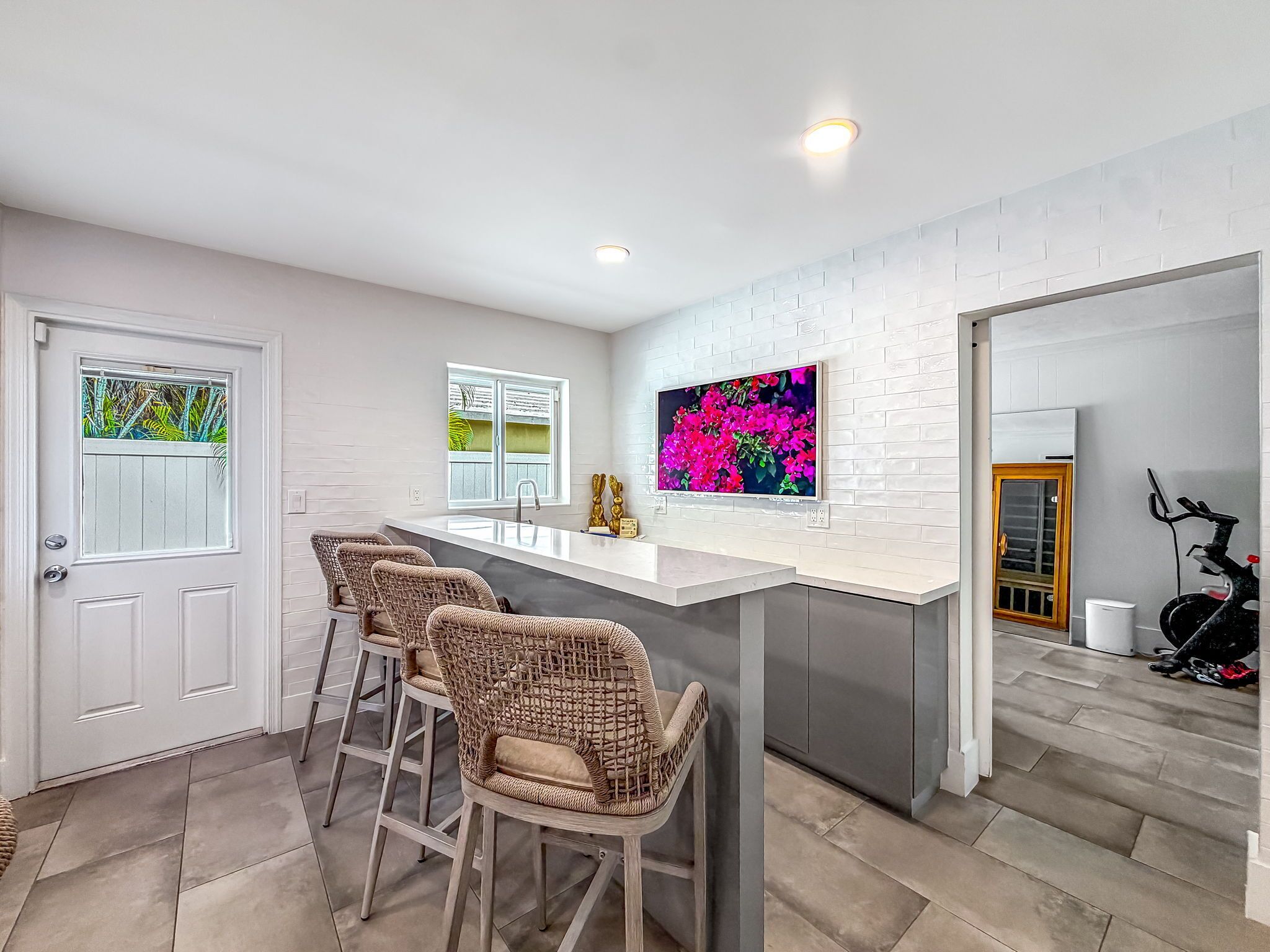 A modern kitchen with a white countertop, bar stools, and a large window.