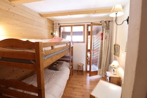 A bunk bed room with a wooden floor, a small stool, a table, and a window with curtains. - 2nd floor, balcony, parking, tv, 35m², Les Gets (Les Gets)