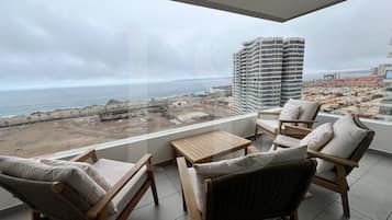 Varanda com vista para a praia e para a paisagem urbana, mobiliada com cadeiras de vime e uma mesa pequena.