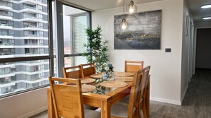 A dining area with a glass table, wooden chairs, woven placemats, and a potted plant.