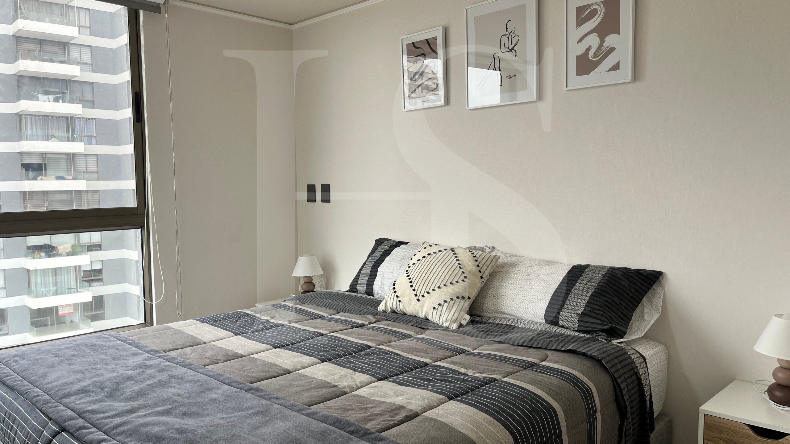 A bedroom with a bed, a window, and three framed artworks on the wall.