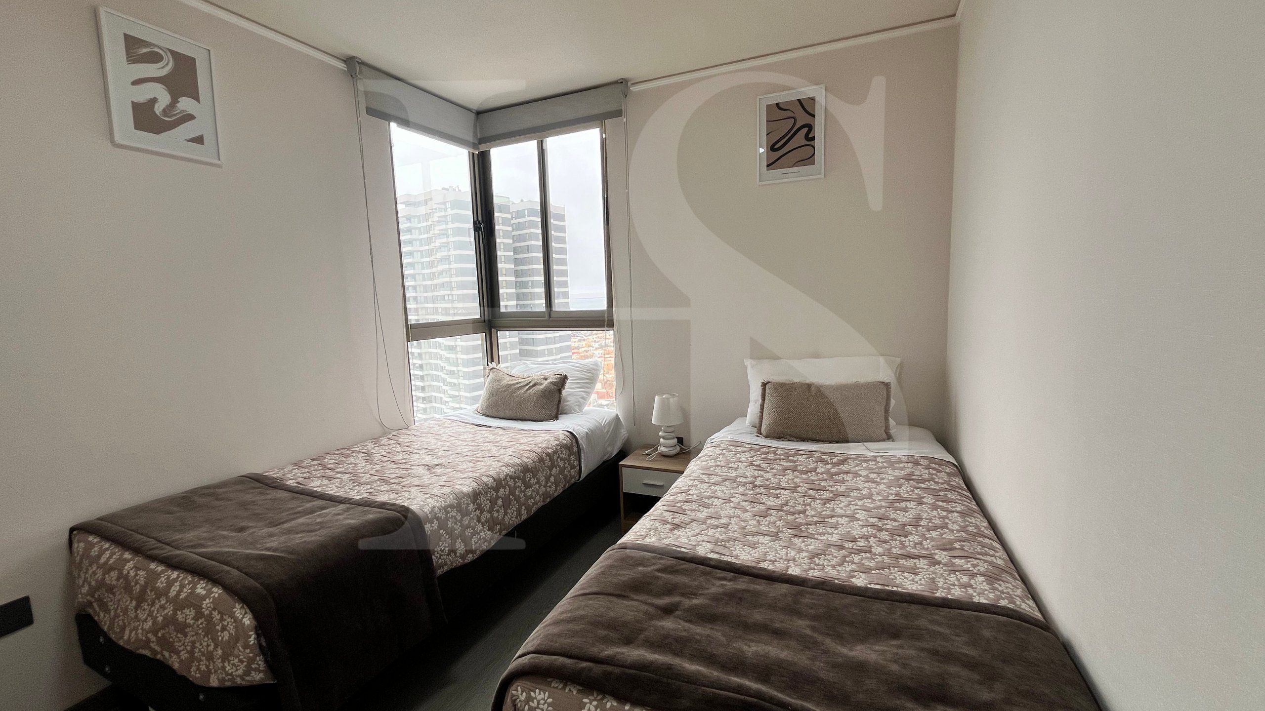 A small, compact room with two single beds, a window with a view of buildings, and a wall-mounted artwork.