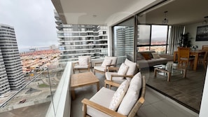 A balcony with a view of a cityscape, furnished with chairs and a sofa, and a dining area with a table and chairs.