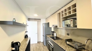 A compact kitchen with a built-in microwave, a coffee maker, and a stainless steel refrigerator.