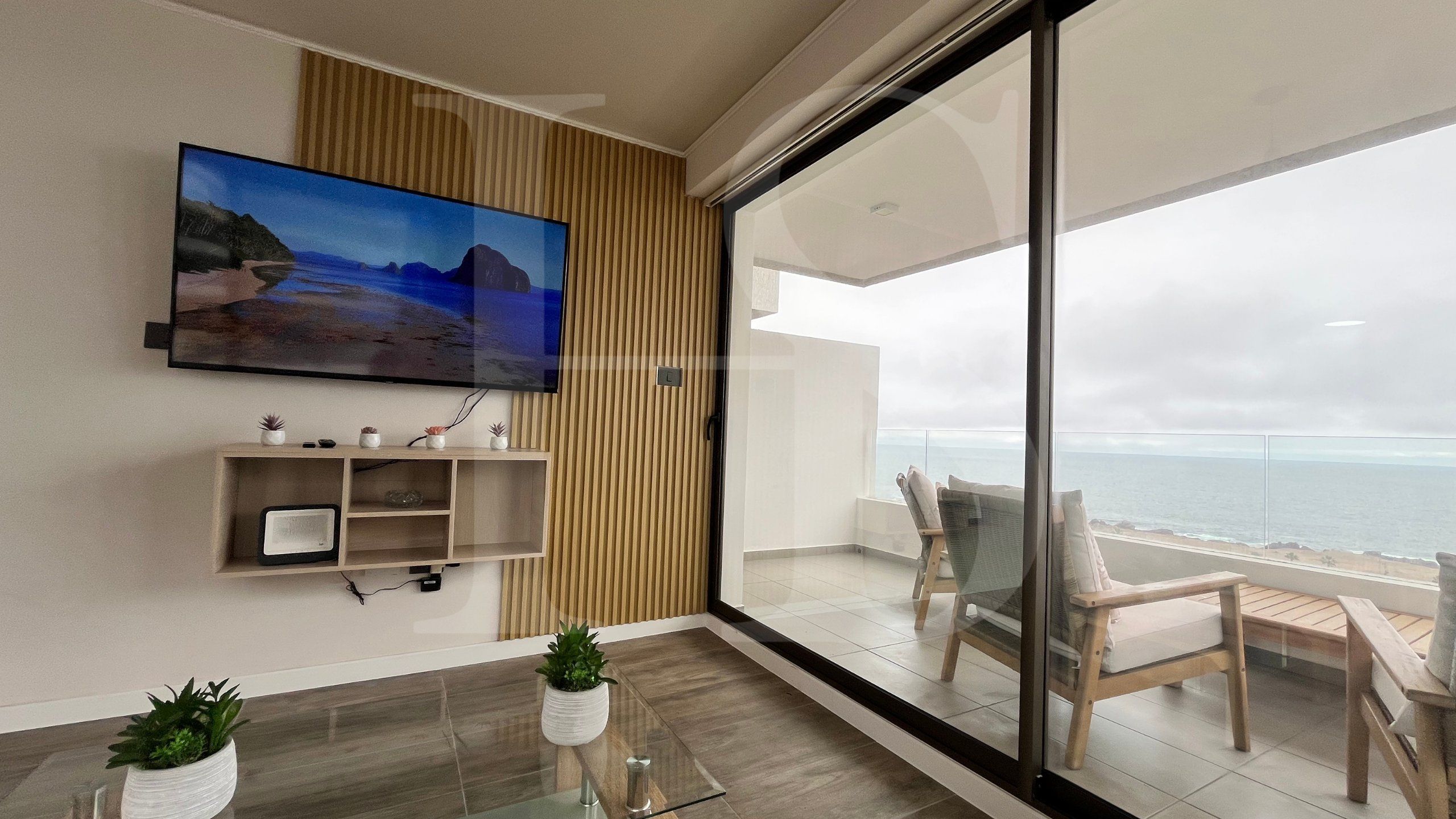 Sala de estar moderna com televisão de tela plana, painel de parede de madeira e varanda com vista para o mar.