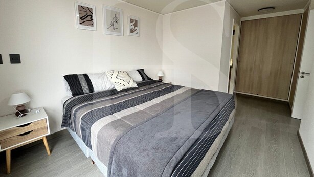 Ein Schlafzimmer mit Bett, Nachttisch, Lampe und Kunstwerk an der Wand.