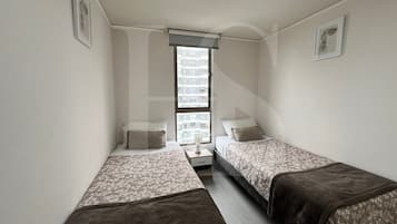 Una habitación pequeña y estrecha con dos camas individuales, una mesita de noche y una ventana.