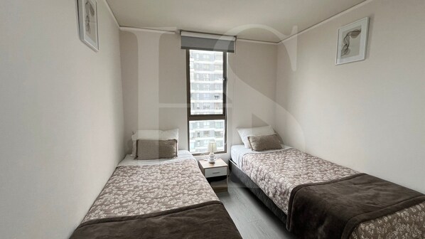 A small, narrow room with two single beds, a nightstand, and a window.