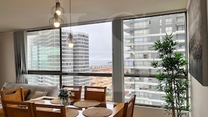Una sala de estar moderna con comedor, ventanas amplias y vistas a rascacielos.
