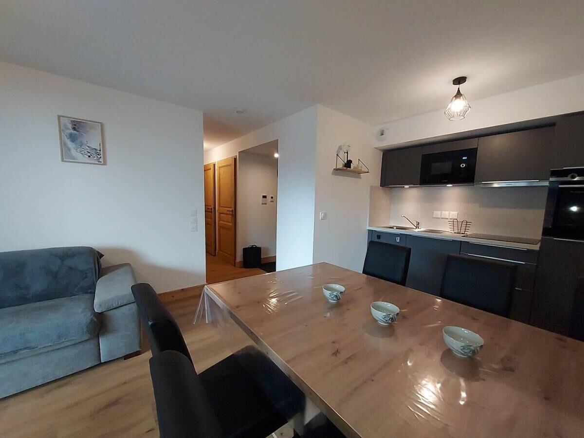 A modern kitchen with a dining table, chairs, and a grey sofa.