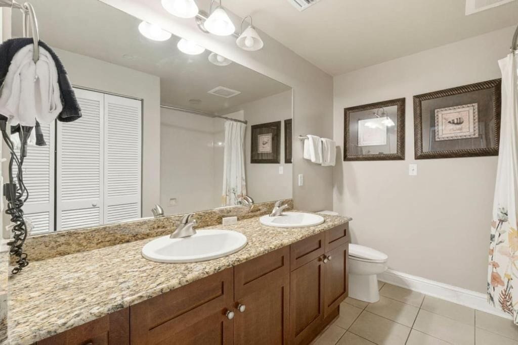 A bathroom with a granite countertop, two sinks, a toilet, and a shower curtain.
