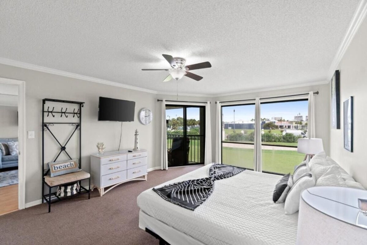 A bedroom with a bed, a TV, a balcony with a view, and a ceiling fan.