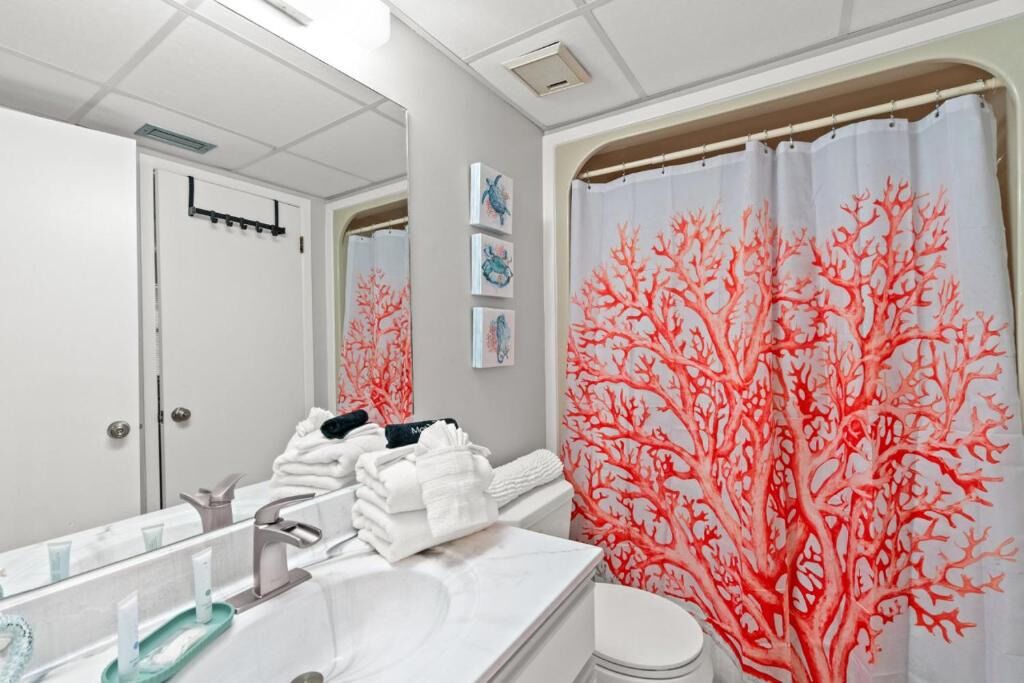 A bathroom with a white sink, a mirror, a toilet, and a shower curtain with a coral tree design.