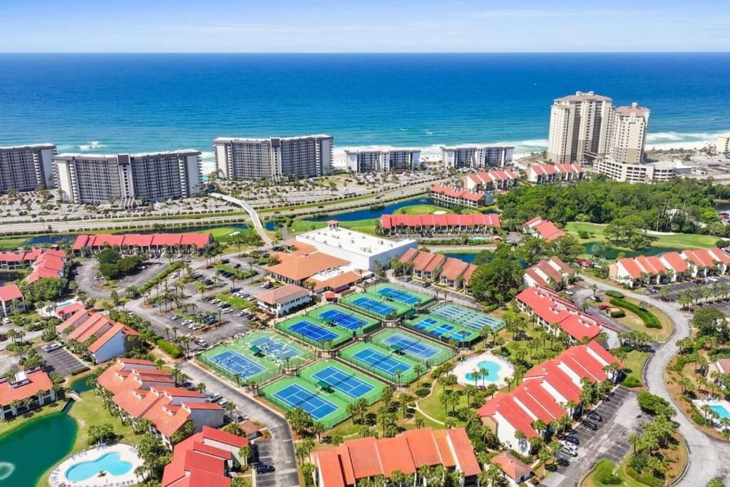 Een resort met verschillende tennisbanen, een zwembad en uitzicht op het strand.