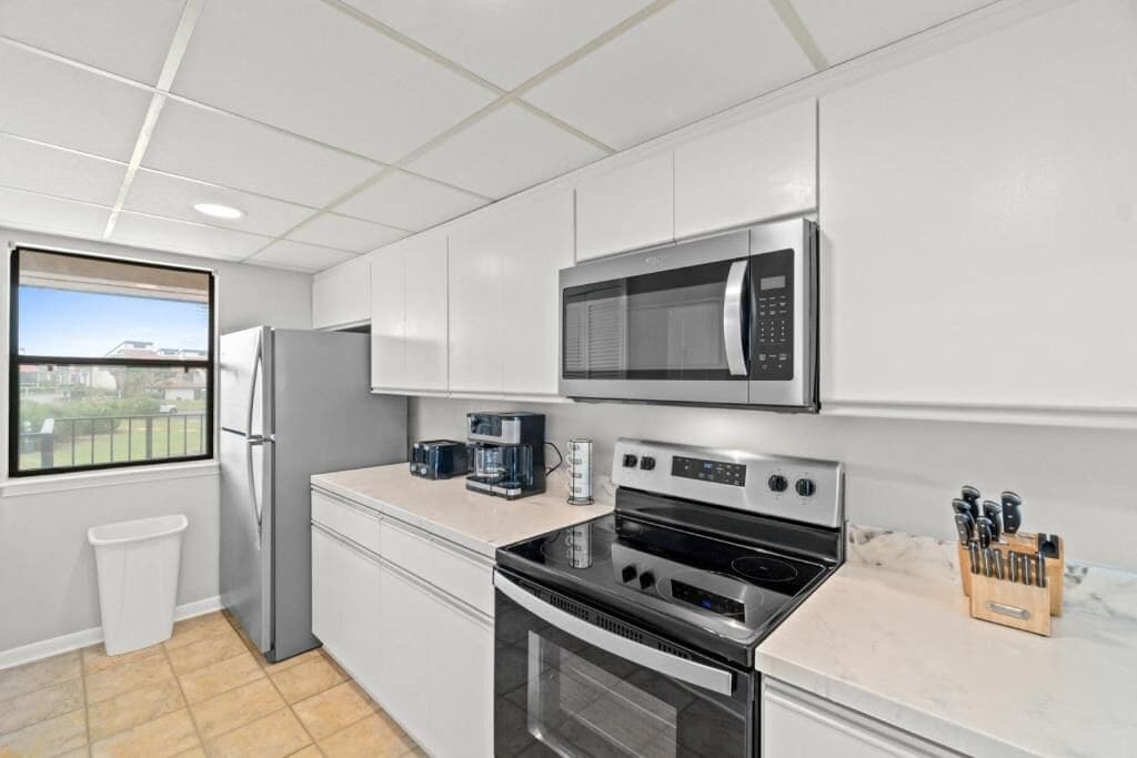 A modern kitchen with stainless steel appliances, a window with a view, and a trash bin.