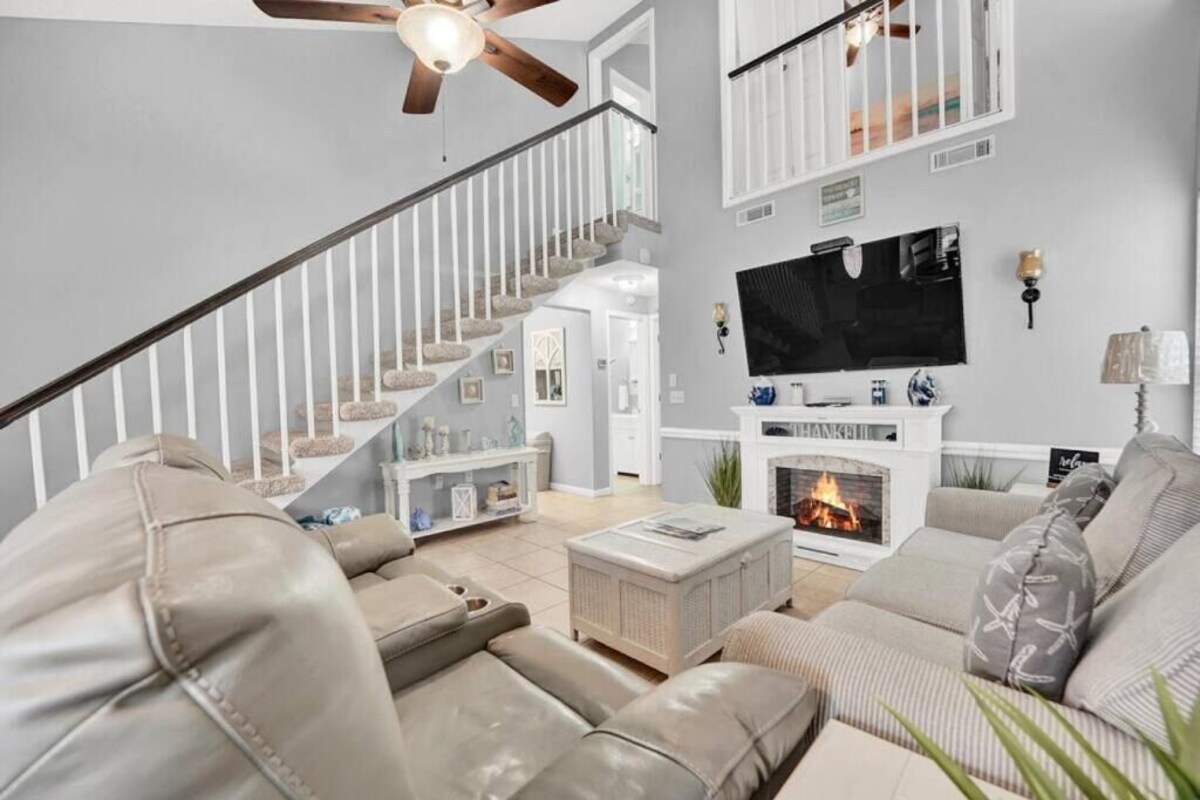 A living room with a fireplace, a staircase, and a television mounted on the wall.