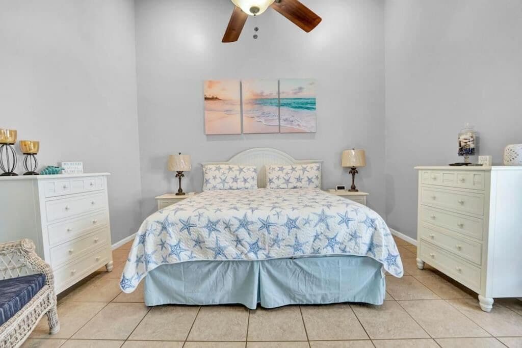 A bedroom with a bed, two nightstands, a dresser, a chair, and a ceiling fan.