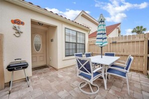 A patio with a white table and blue chairs, a grill, and a striped umbrella. - Horizon South (Panama City Beach)