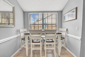 A dining area with a round table and four chairs, a window with blinds, and a framed picture on the wall. - Horizon South (Panama City Beach)