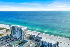 A beachfront hotel with multiple high-rise buildings, a parking area, and a beach. - Nautical Watch (Panama City Beach)