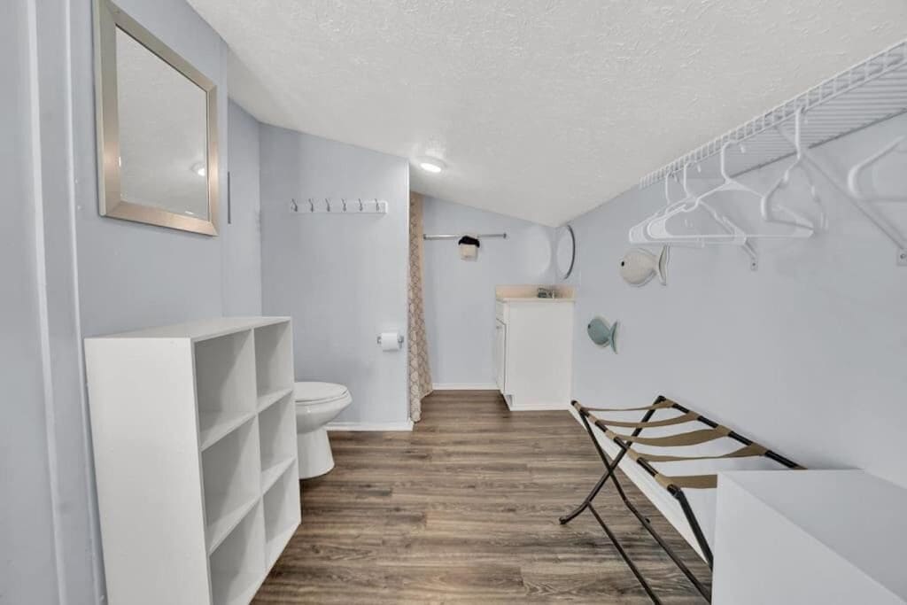 Ein Badezimmer mit einem weißen Waschbecken, einer Toilette und Regalen, einem Holzboden und einem Handtuchhalter.