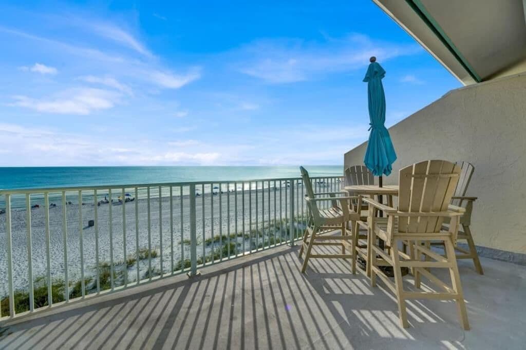 Un balcón con vista a la playa, sillas de madera y una mesa.