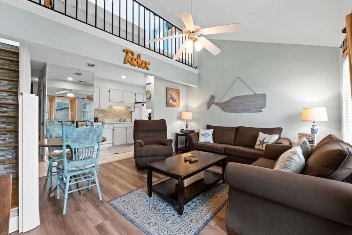 A spacious living area with a ceiling fan, a dining table with chairs, and a kitchen in the background.