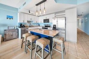 A modern kitchen with white cabinets, a central island with stools, stainless steel appliances, and a hanging light fixture. - Laketown Wharf (Panama City Beach)