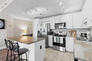 A modern kitchen with white cabinetry, stainless steel appliances, and a central island with bar stools. - Laketown Wharf (Panama City Beach)