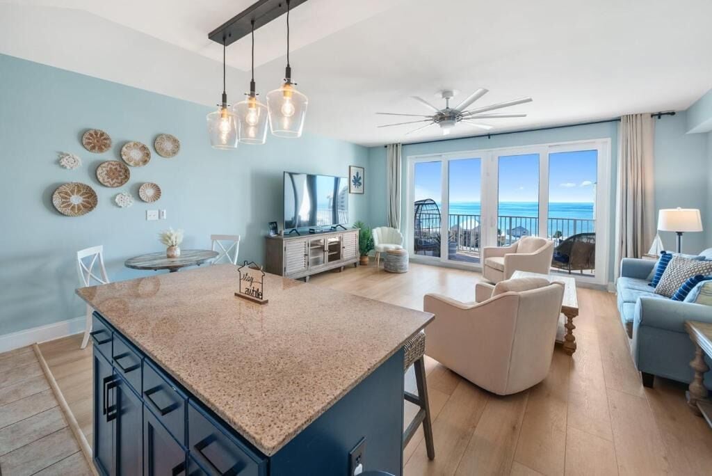 A modern living room with a large island, a ceiling fan, and a view of the ocean.