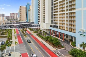 A multi-story hotel with a red and white color scheme, a pedestrian bridge, and a parking area with cars. - Majestic (Panama City Beach)