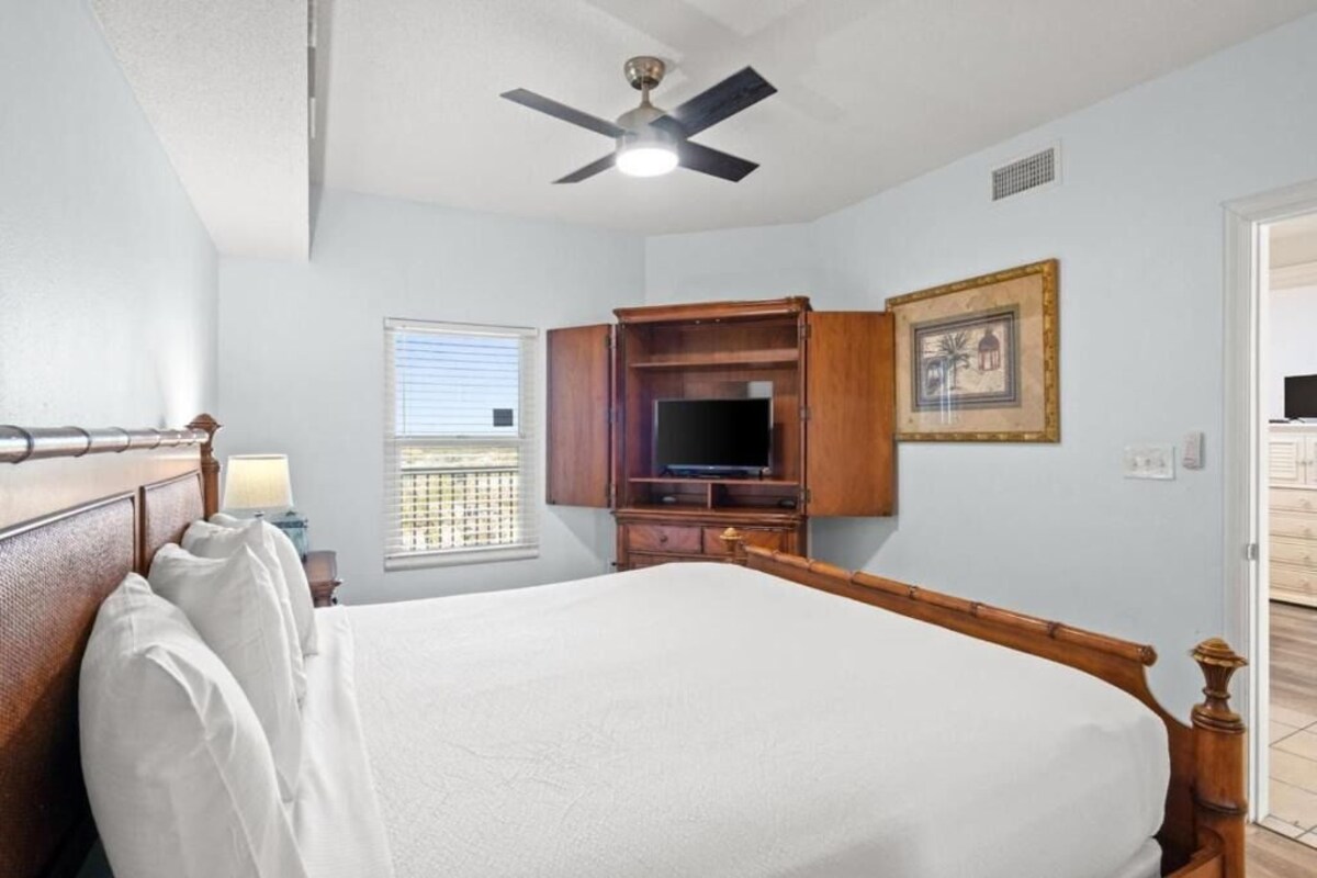 A bedroom with a bed, a ceiling fan, a television, and a window.