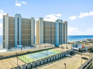 A high-rise residential building with multiple balconies, a rooftop tennis court, and a view of the ocean. - Majestic (Panama City Beach)