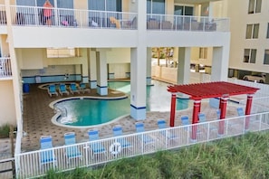 A multi-level hotel with a swimming pool, lounge chairs, and a covered seating area. - Majestic (Panama City Beach)